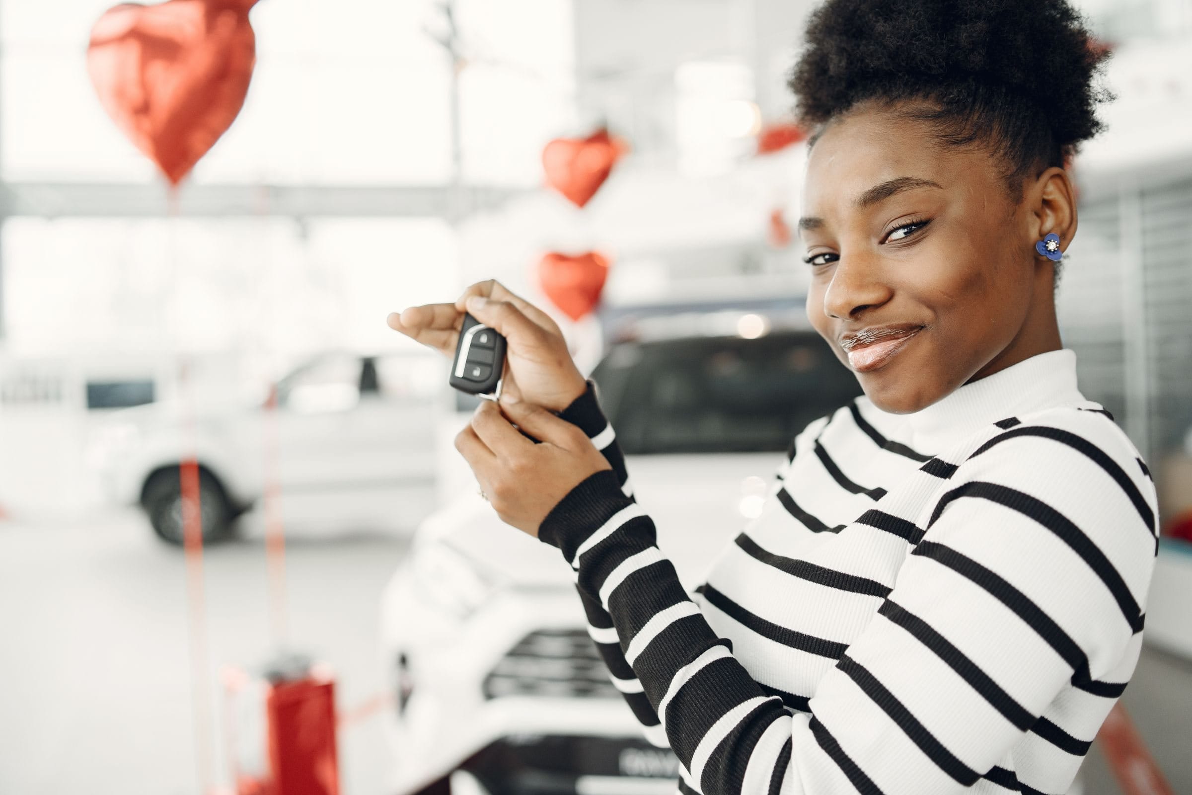 A smiling woman holds up the key to her newer car in a bright dealership showroom